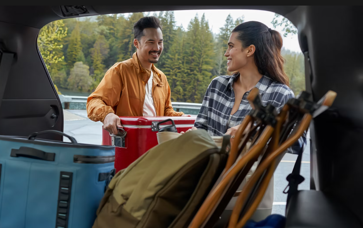 Couple standing in front of the open cargo door of the 2024 Toyota Grand Highlander with camping gear